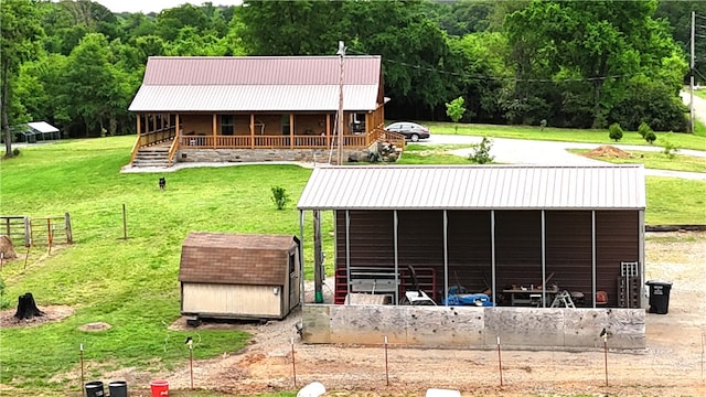 rear view of property featuring a lawn, a view of trees, an outbuilding, and metal roof