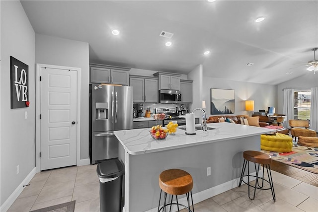 kitchen featuring gray cabinets, a kitchen breakfast bar, a sink, open floor plan, and stainless steel appliances
