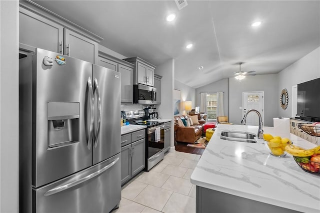 kitchen with stainless steel appliances, gray cabinets, open floor plan, and a sink