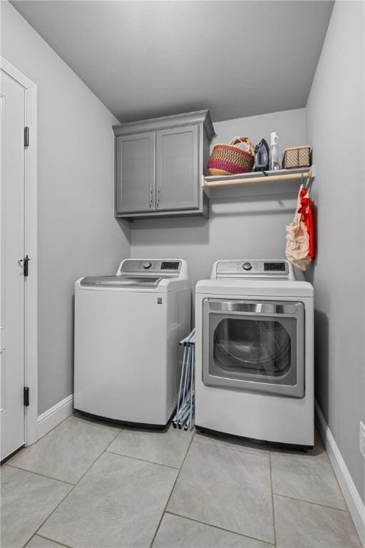 washroom featuring cabinet space, baseboards, washing machine and dryer, and light tile patterned floors