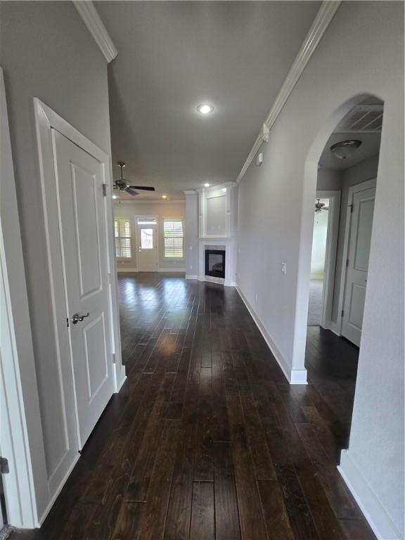 hallway with dark wood-style flooring, baseboards, ornamental molding, and arched walkways