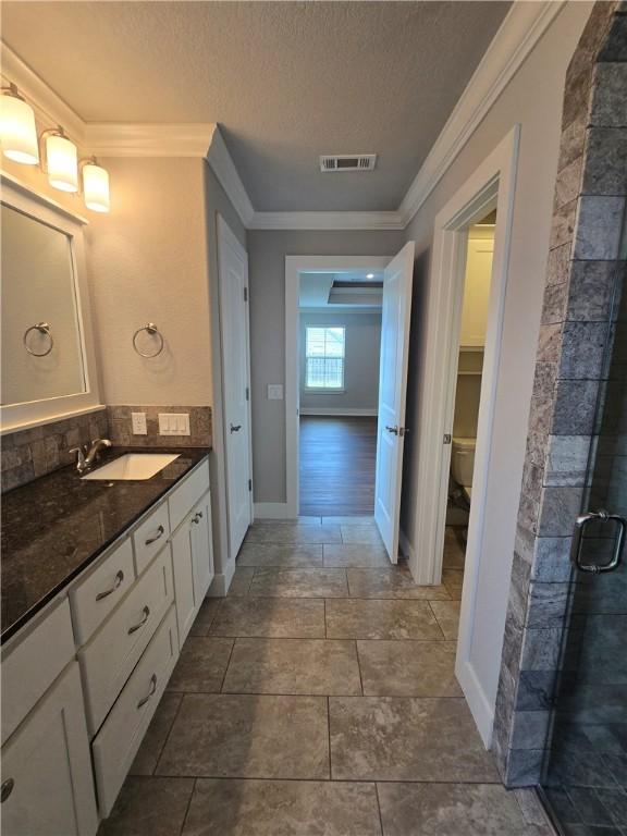 bathroom with crown molding, vanity, toilet, a textured ceiling, and visible vents