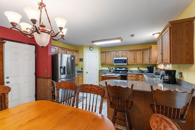 kitchen with visible vents, a peninsula, a chandelier, a sink, and stainless steel appliances