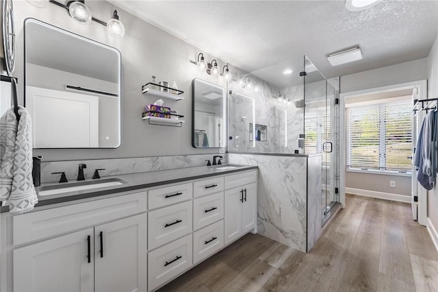 bathroom with double vanity, a marble finish shower, a sink, and wood finished floors