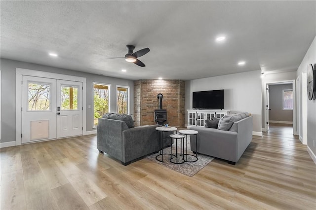 living area featuring baseboards, ceiling fan, a wood stove, and light wood-type flooring