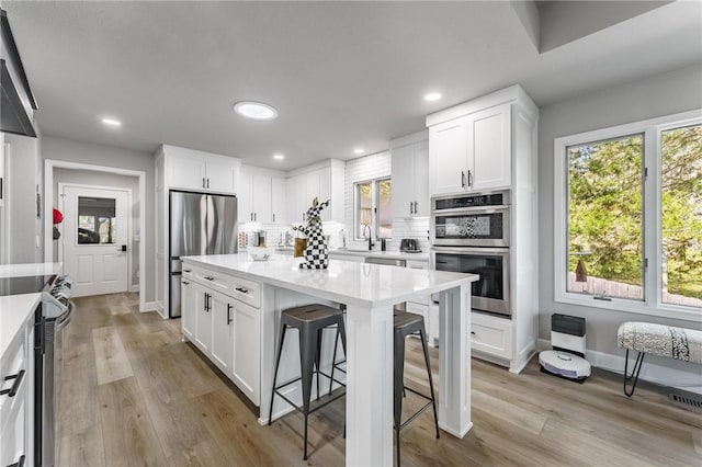 kitchen featuring decorative backsplash, a kitchen bar, white cabinets, a sink, and appliances with stainless steel finishes