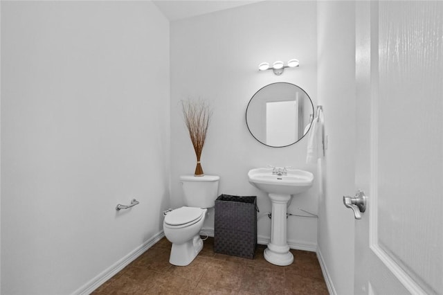 half bathroom with toilet, baseboards, a sink, and tile patterned flooring