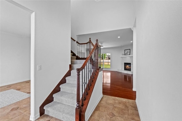 stairway featuring a glass covered fireplace, tile patterned floors, baseboards, and recessed lighting
