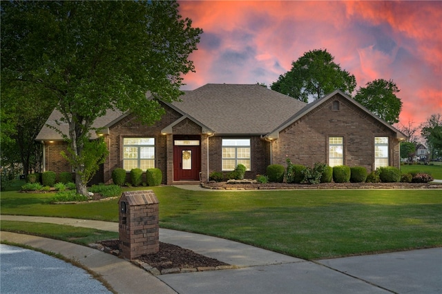 view of front of house featuring a yard, brick siding, and roof with shingles