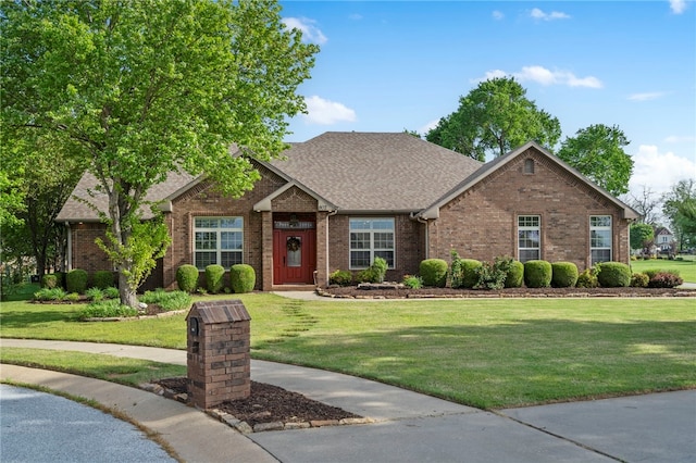 view of front of home featuring a shingled roof, a front yard, and brick siding