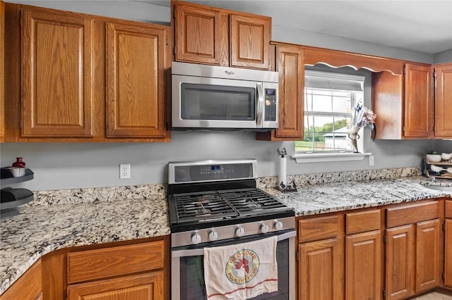 kitchen with brown cabinets, appliances with stainless steel finishes, and light stone counters