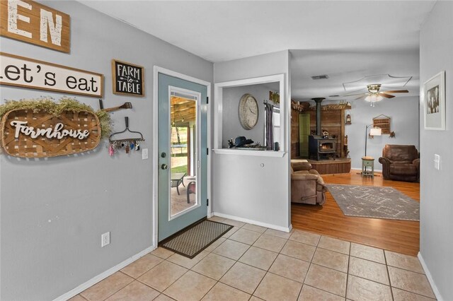 foyer with visible vents, a wood stove, light tile patterned flooring, baseboards, and ceiling fan
