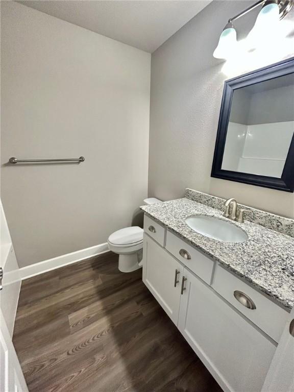 bathroom featuring toilet, baseboards, wood finished floors, and vanity