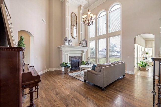 living room with visible vents, a high end fireplace, a towering ceiling, wood finished floors, and ornamental molding