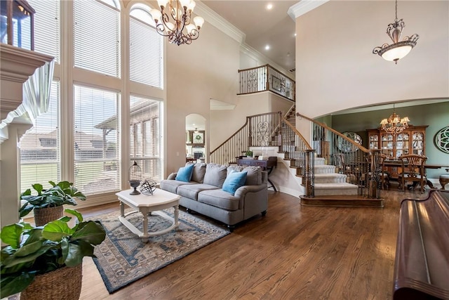 living area featuring ornamental molding, stairs, a high ceiling, arched walkways, and a notable chandelier