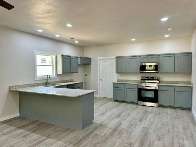 kitchen featuring stainless steel appliances, baseboards, light wood finished floors, and a peninsula