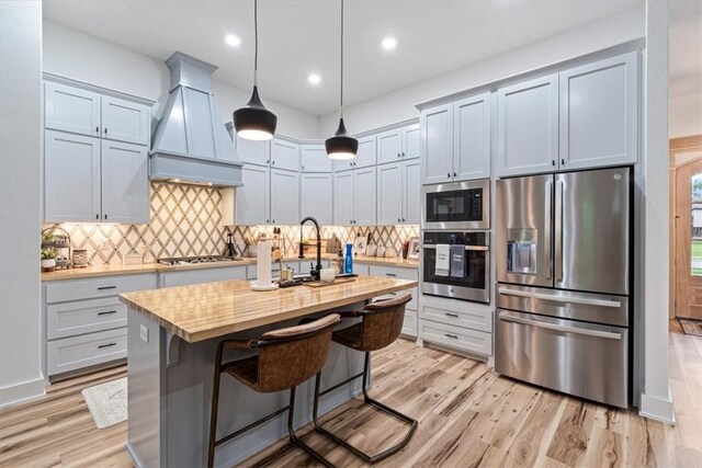 kitchen with stainless steel appliances, custom exhaust hood, a sink, and light wood-type flooring