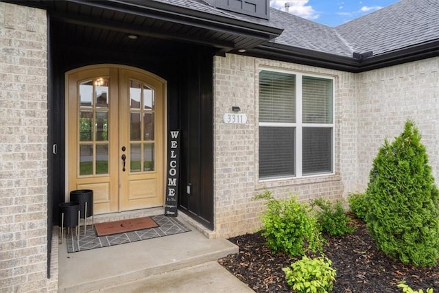 entrance to property featuring brick siding, roof with shingles, and french doors