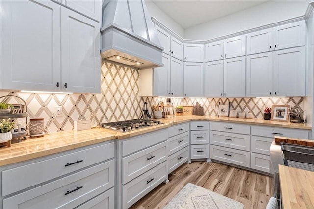 kitchen featuring white cabinets, light wood-style floors, wood counters, decorative backsplash, and custom range hood