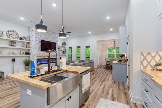 kitchen featuring a kitchen island with sink, a ceiling fan, a fireplace, a sink, and butcher block counters