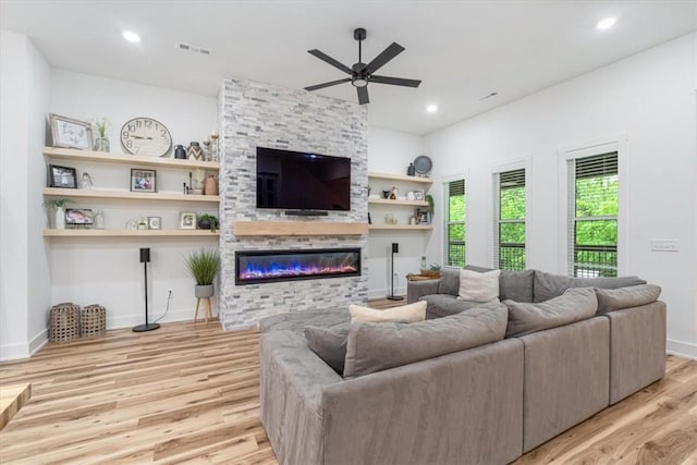 living area featuring a ceiling fan, visible vents, a fireplace, baseboards, and light wood finished floors