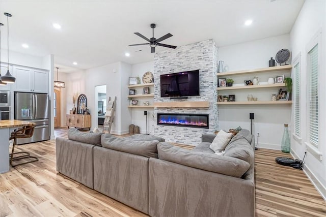 living room with a fireplace, a ceiling fan, recessed lighting, and light wood-style flooring
