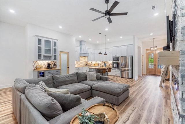 living area featuring visible vents, baseboards, beverage cooler, ceiling fan, and light wood-type flooring