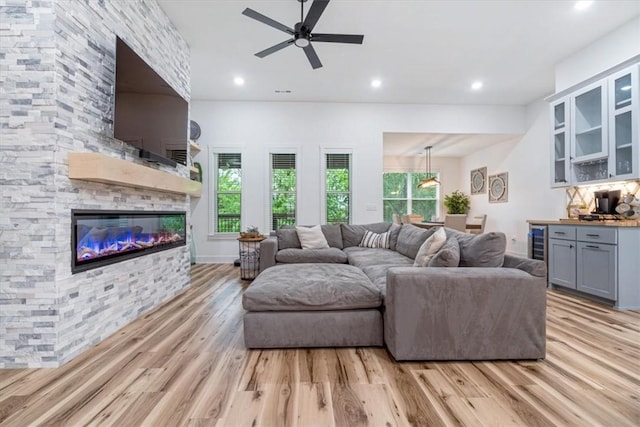 living area featuring recessed lighting, ceiling fan, a stone fireplace, and light wood-type flooring