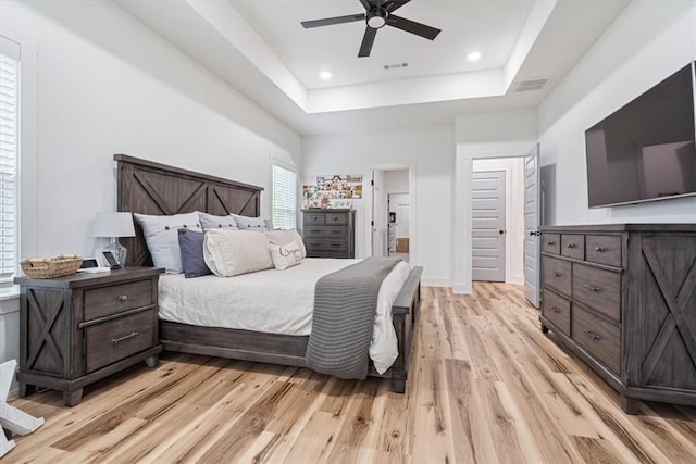 bedroom with light wood-style floors, a tray ceiling, recessed lighting, and visible vents