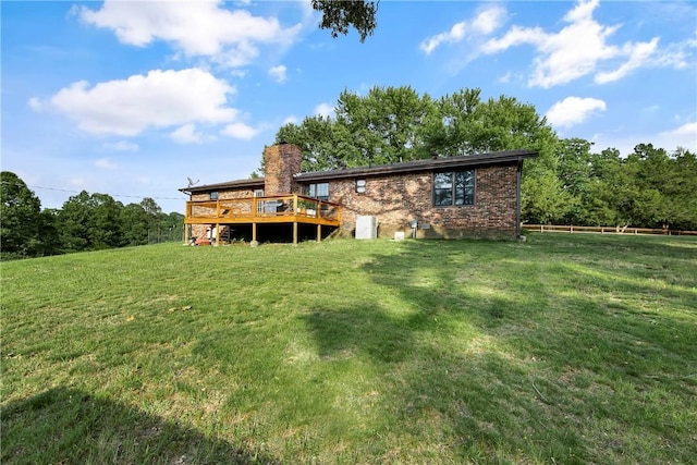 back of house featuring fence, a deck, a chimney, brick siding, and a lawn
