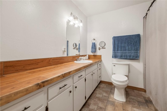 full bathroom featuring toilet, baseboards, stone finish flooring, and vanity