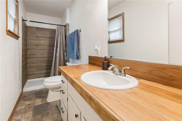 bathroom featuring vanity, toilet, baseboards, stone finish flooring, and a tile shower