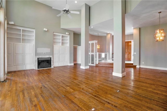 unfurnished living room featuring wood finished floors, a tile fireplace, baseboards, ceiling fan with notable chandelier, and a high ceiling