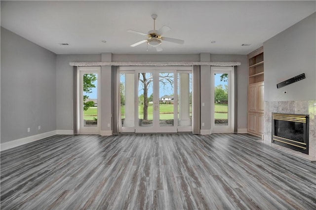 unfurnished living room featuring a high end fireplace, baseboards, ceiling fan, and wood finished floors