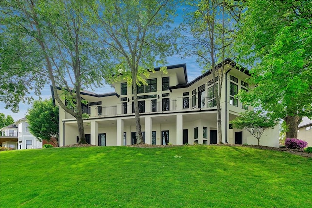 rear view of property featuring a lawn, a balcony, and stucco siding