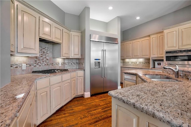 kitchen with dark wood-style flooring, cream cabinetry, tasteful backsplash, a sink, and stainless steel appliances
