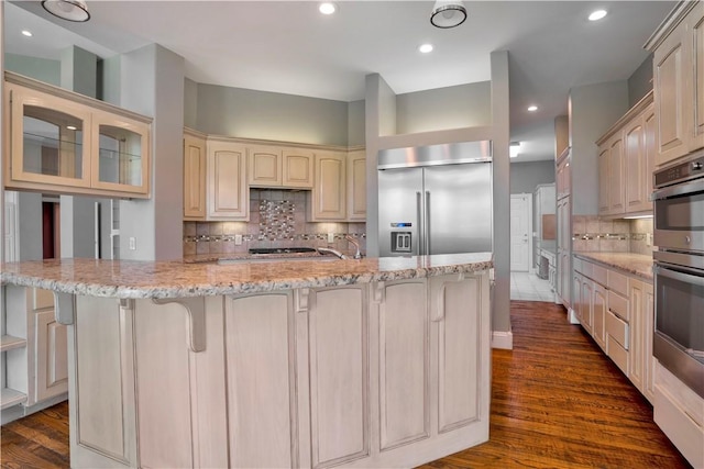 kitchen featuring decorative backsplash, dark wood-style flooring, a kitchen bar, light stone counters, and stainless steel appliances
