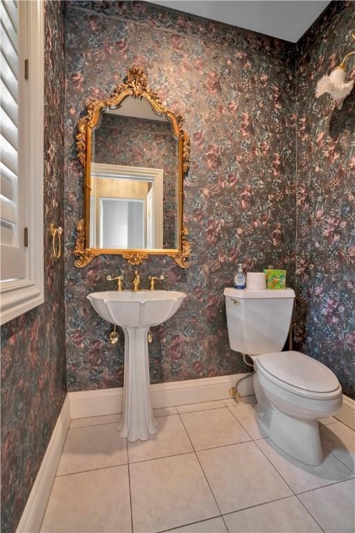 half bath with toilet, tile patterned floors, a sink, and baseboards