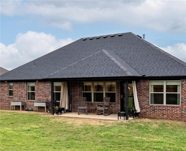 rear view of house featuring brick siding, a shingled roof, a patio area, and a lawn