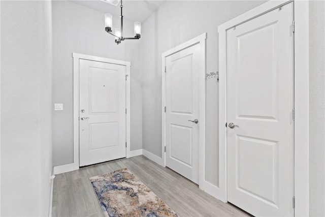 doorway to outside with baseboards, light wood-style flooring, and a notable chandelier