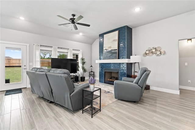 living area featuring baseboards, ceiling fan, a tile fireplace, light wood finished floors, and vaulted ceiling
