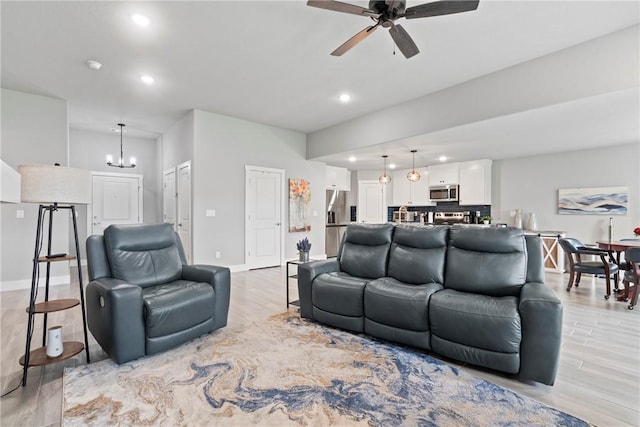living room with recessed lighting, light wood finished floors, ceiling fan with notable chandelier, and baseboards