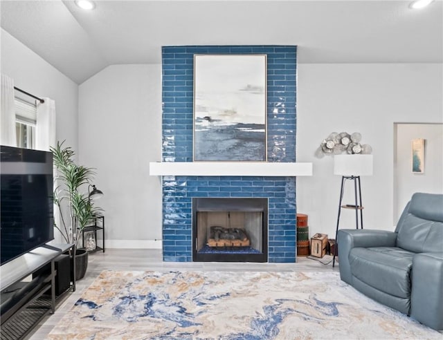 living room featuring wood finished floors, lofted ceiling, a fireplace, baseboards, and recessed lighting