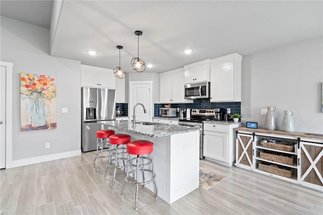 kitchen with a breakfast bar area, appliances with stainless steel finishes, light stone countertops, a sink, and light wood finished floors