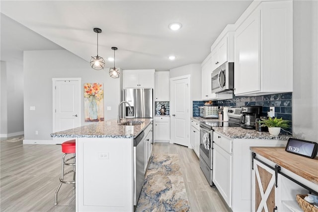 kitchen with appliances with stainless steel finishes, tasteful backsplash, light stone countertops, a sink, and white cabinets