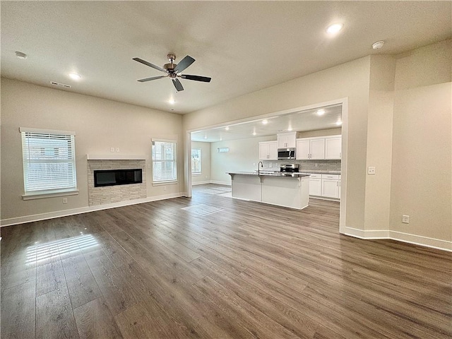 unfurnished living room featuring dark wood-type flooring, a ceiling fan, baseboards, and plenty of natural light