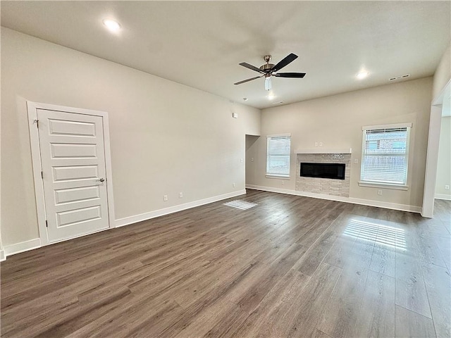 unfurnished living room featuring visible vents, a fireplace, baseboards, a ceiling fan, and dark wood finished floors