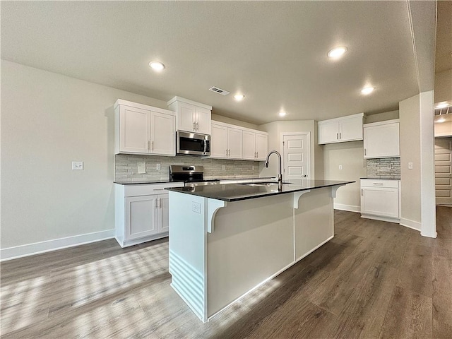 kitchen featuring visible vents, dark countertops, dark wood-style floors, a sink, and stainless steel appliances