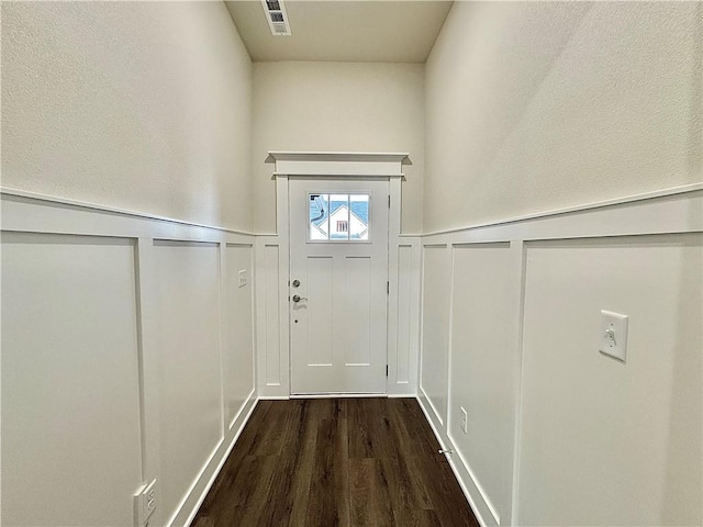 doorway with wood finished floors, wainscoting, and a decorative wall