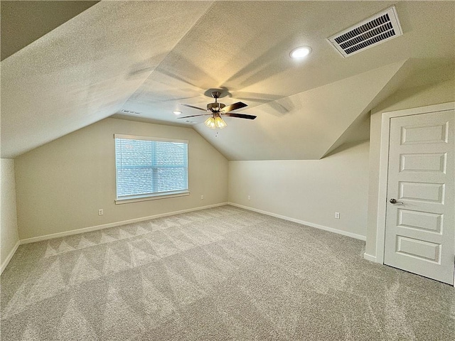 additional living space featuring a textured ceiling, visible vents, baseboards, lofted ceiling, and carpet